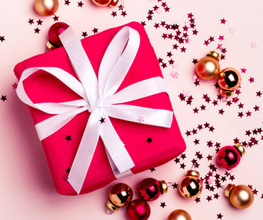 Cadeau rouge sur fond rose avec des boules de Noël rouges et dorées et des étoiles scintillantes